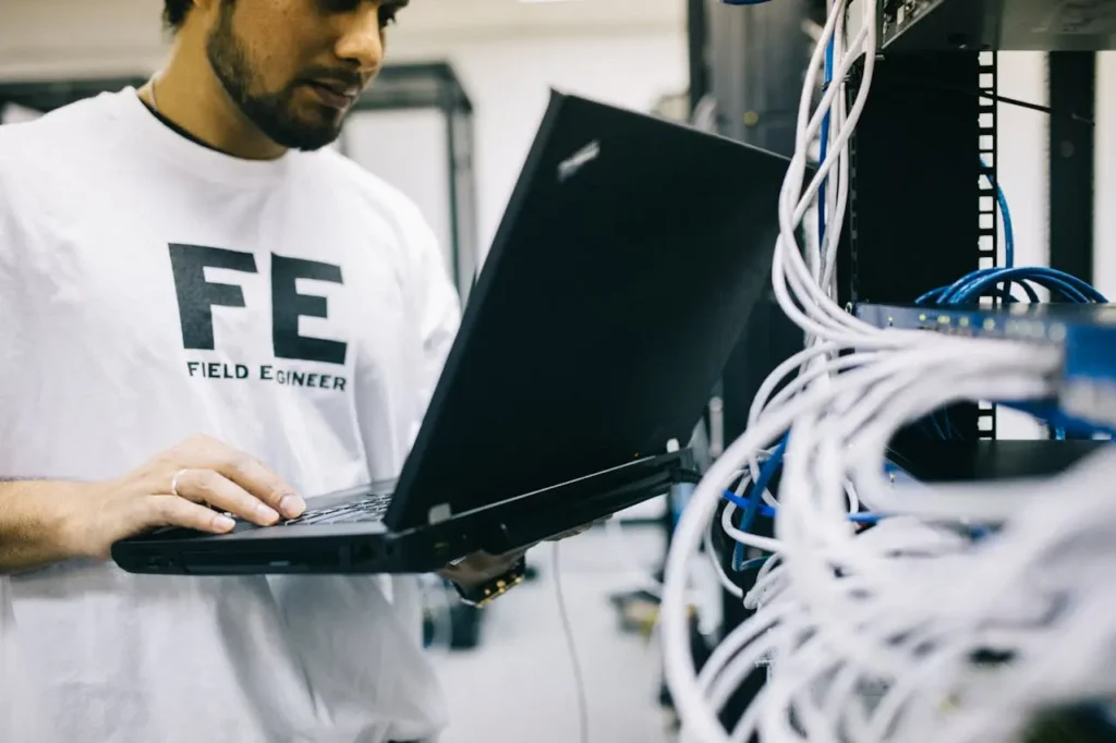 Serious ethnic field engineer examining hardware and working on laptop